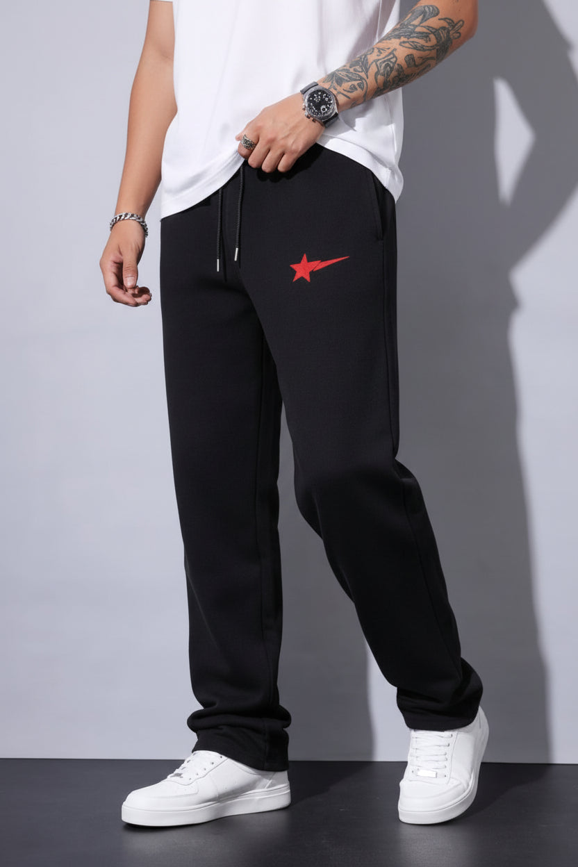 Person wearing black pants with a red star logo and white sneakers on a gray background