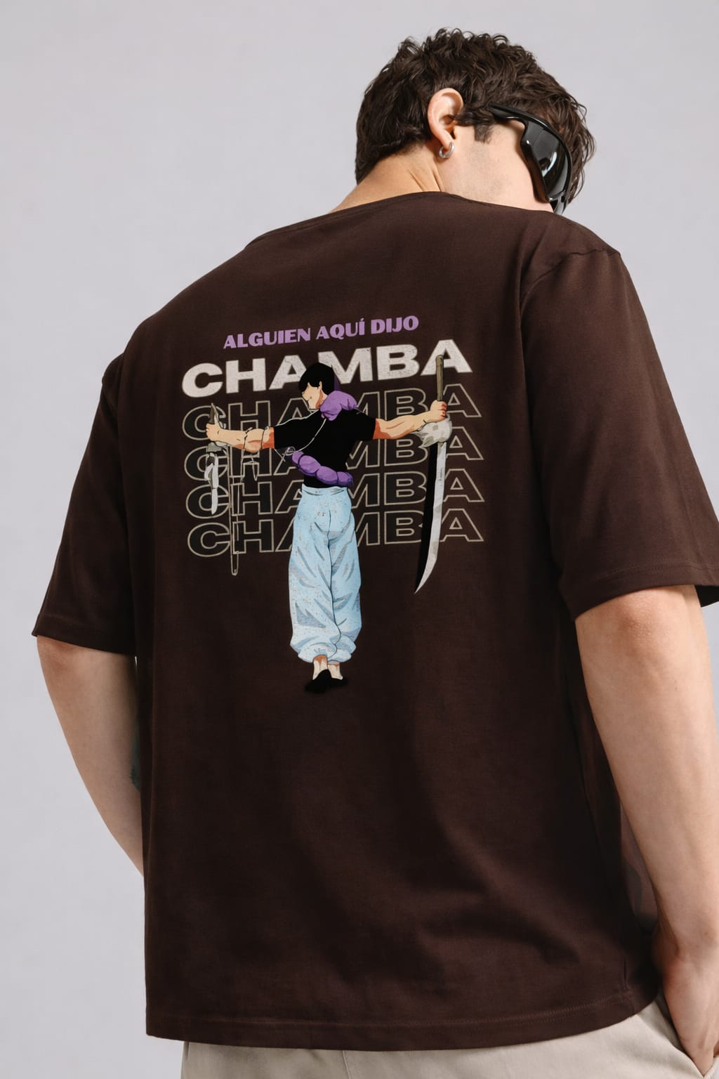 Person wearing a brown t-shirt with graphic design and text on the back, standing against a plain background.